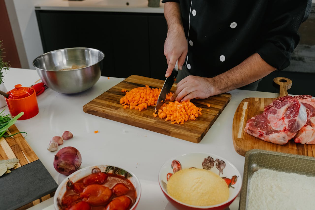 who-we-are Chef chops carrots on a cutting board surrounded by fresh ingredients in a modern kitchen.